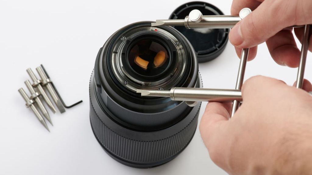 Technician opening a lens with a spanner wrench on the European Camera Repair bench