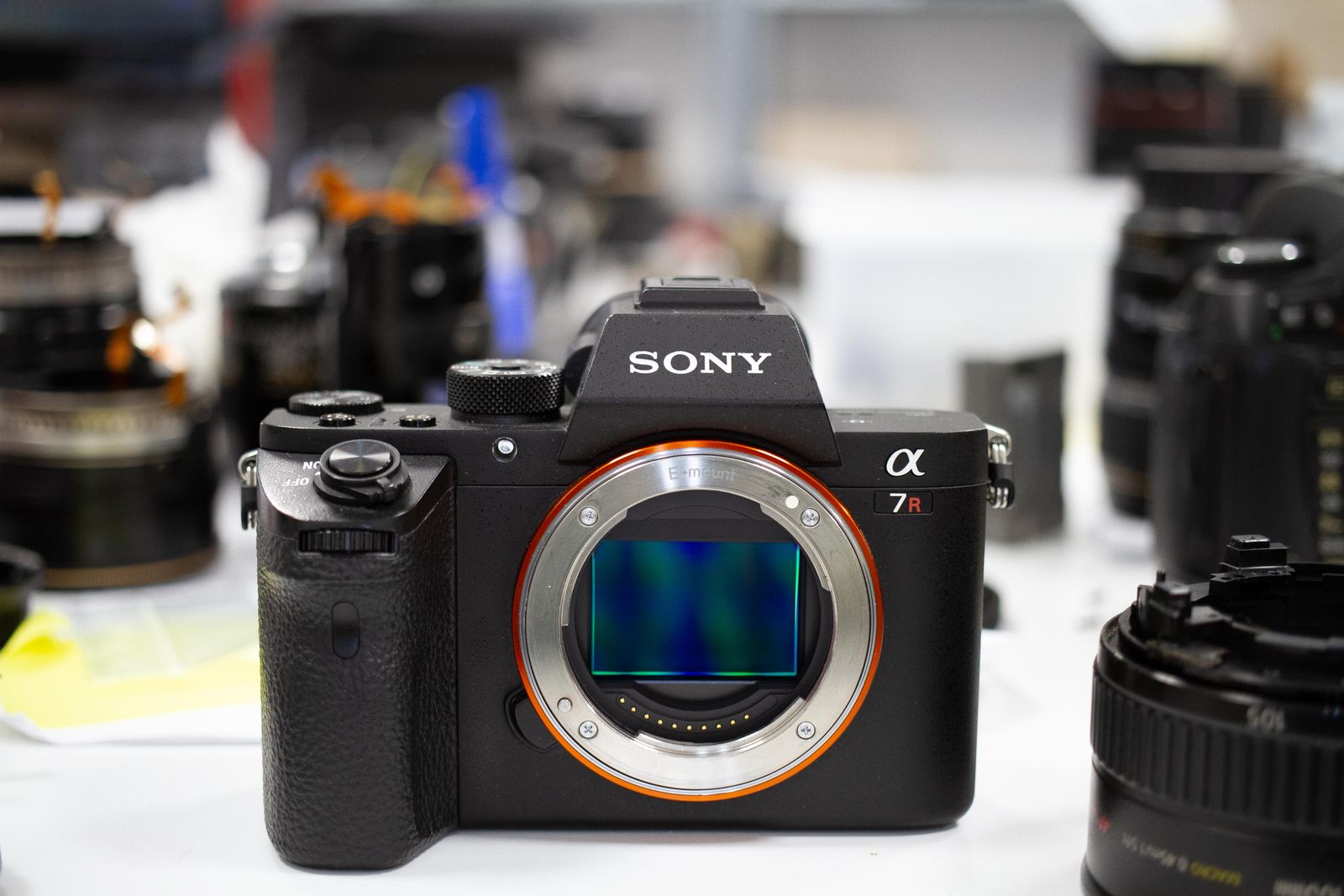 Sony A7R II with the sensor exposed on the European Camera Repair bench, surrounded by lenses under repair